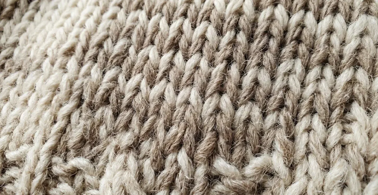 Gros plan extrême sur la texture d'une maille en laine naturelle révélant la structure des fibres torsadées et les irrégularités naturelles du tricot