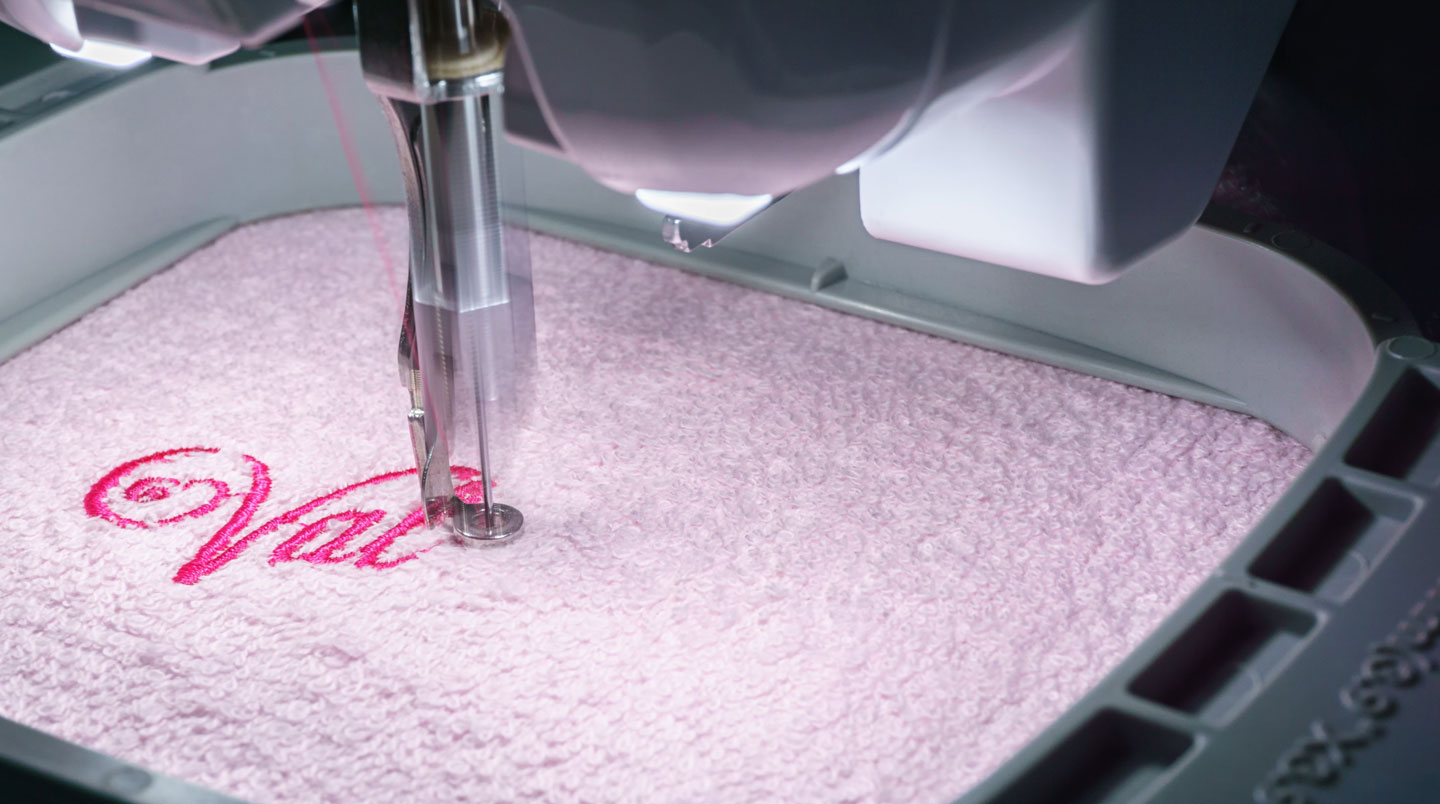 Machine à broder industrielle multi-aiguilles en action sur textile éponge blanc dans atelier français de personnalisation